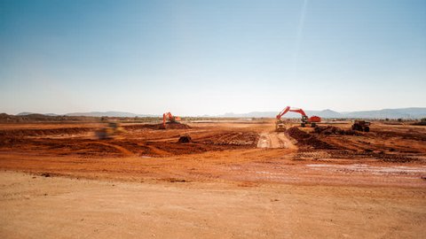 Static pan timelapse of a construction site on a mine while earthworks is in progress with heavy load machinery, trucks and tippers close to action.