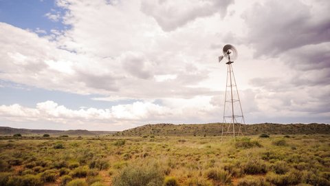 Static timelapse of a windmill with cumulus clouds and formations blowing frantically in the wind against a dark and stormy sky in a typical Karoo landscape.