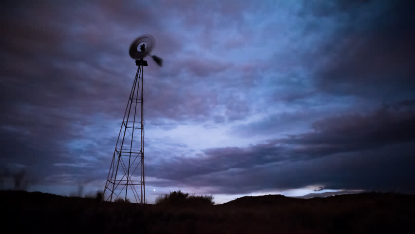 Static timelapse of a franticly blowing windmill silhouetted against a dramatic and stormy sky with clouds, thunder and lightning, clearing up later in the shot.