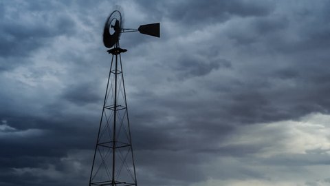 Static timelapse of a franticly blowing windmill silhouetted against a dramatic and stormy sky with thunder and lightning while the clouds are constantly changing and blows from right to left.
