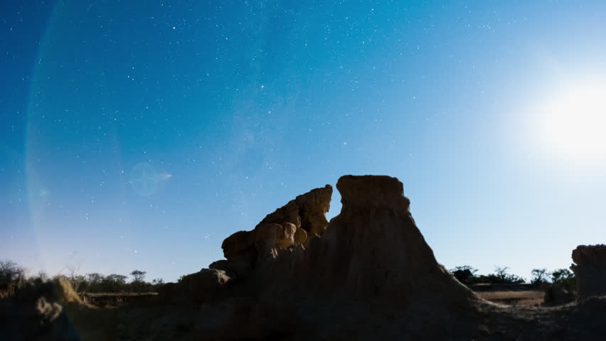 Linear, push-in night timelapse of abstract landscape with silhouette eroded rocks while the moon is setting and the Milky Way moves into the frame.