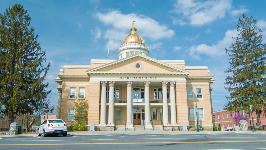 Traffic on Main Street in front of the Historic Courthouse in Downtown Hendersonville, NC featuring a Passing Car and Green Trees in front of a Blue Sky Background on a Sunny Day.