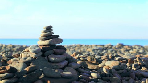 Close-up shot of finishing stone pyramid on the coast. Stony shore, sea and blue sky in bakground