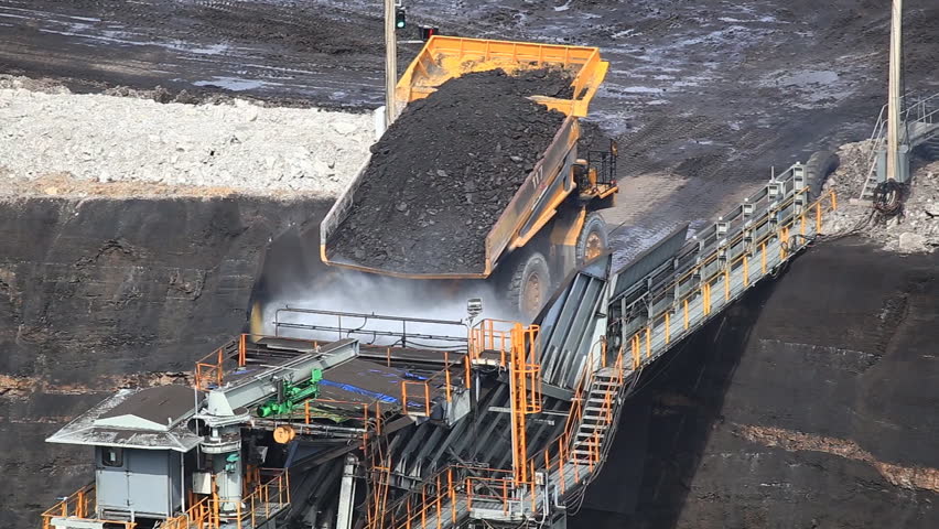 Heavy construction tipper trucks dump coal to the conveyor at coal mine 