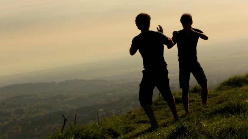 Silhouettes of two fighters on sunset yellow background: martial art, fight