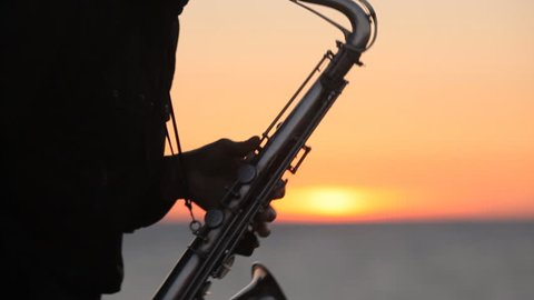 The silhouette of a musician masterly playing saxophone on the seacoast at amazing sunset