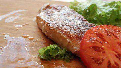 Grilled meat pork steaks with tomatoes and lettuce served by forks on a wooden board.