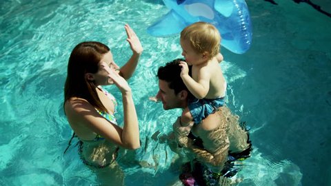 Attractive young Caucasian parents enjoying time playing baby son with inflatable toy outdoor swimming pool vacation rental shot on RED EPIC