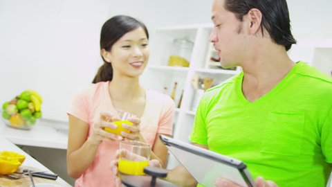 Upper body young multi ethnic couple bright casual clothing wireless tablet home kitchen counter drinking fresh squeezed orange juice shot on RED EPIC