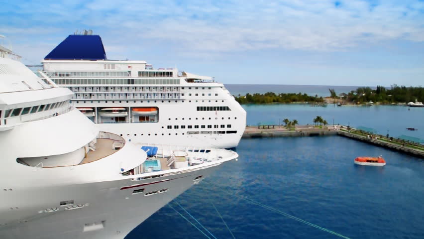 A single lifeboat travels past two large, docked cruise ships in Nassau.