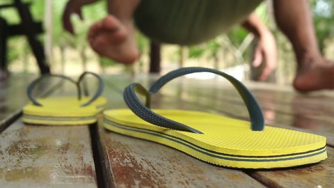 Flip flops or thongs in foreground as a very relaxed man swings on a hammock in the blurred background.