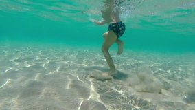 Little boy running in sea to his mother, who helps him swim. Underwater shot.