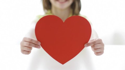 love, home, happiness, childhood and people concept - close-up of smiling girl with red paper heart at home