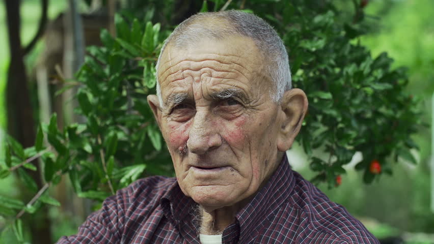 very old person, smiling looks into the camera: green background, countryside