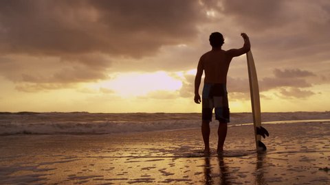Silhouette solitary young male surfer standing sand beach sunrise holding surfboard watching ocean waves shot on RED EPIC