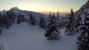 flying upwards over winter forest with the sun setting behind the alps