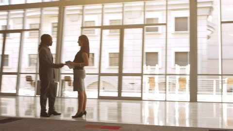 Steadicam Shot of African American man shaking hands with business associate in modern glass office building.