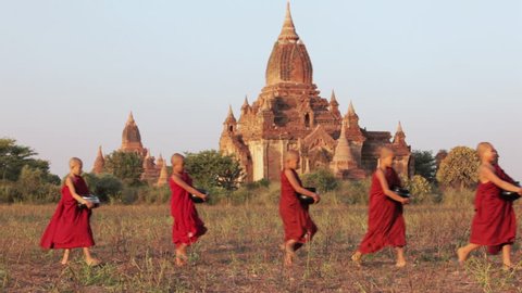 Young Buddhist novice monks walk past a temple in procession carrying alms bowls / Bagan, Myanmar
