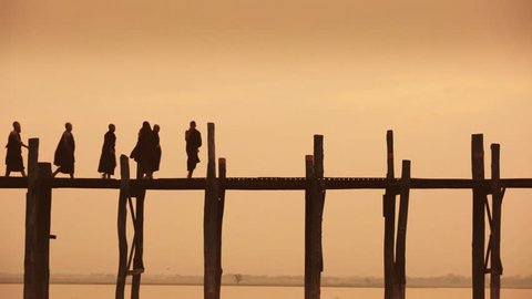 A group of Buddhist monks pass another monk, who playfully kicks one of them, at sunset on U Bein Bridge, the longest teak bridge in the world / Mandalay, Myanmar