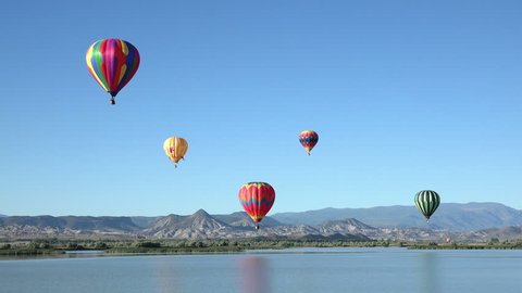 SALINA, UTAH - JUN 2014: Colorful hot air balloon flight over rural lake. Pilot fly slow moving aircraft. Early morning community festival has annual Balloon Fest and competition. Mountain valley.