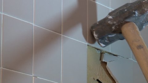 Close up view of sledge hammer pounding and breaking ceramic wall tile during shower renovation project.