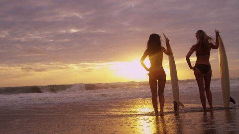 Multi ethnic female surfing friends holding surfboards standing silhouette ocean shallows beach sunset watching waves shot on RED EPIC