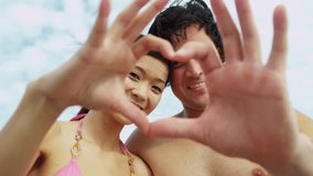 Portrait attractive young Asian Chinese couple head shoulders smiling having fun swimwear beach using hands heart shape filming post selfie social media sites full frame shot on RED EPIC