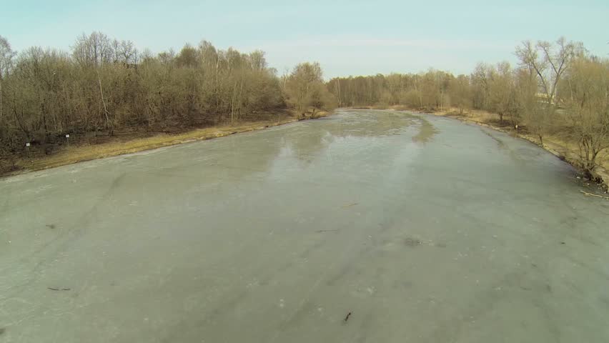 Wet surface of icy pond near forest lit by sunlight at spring day. Aerial view