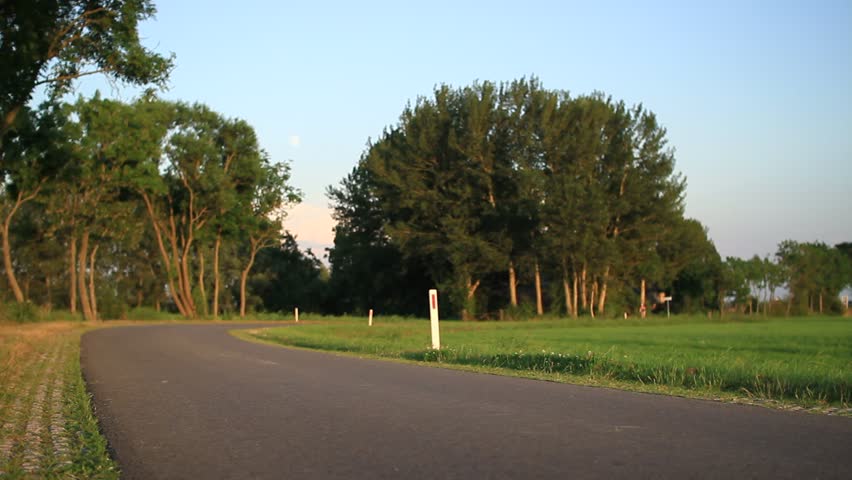 Male road bike racer goes past on a sunny evening in the countryside. 
