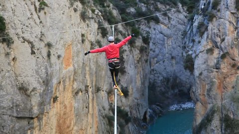 France, 2013. A man tightrope walking over high canyon, trying to keep his balance, starts to swing and falls and hangs from the rope