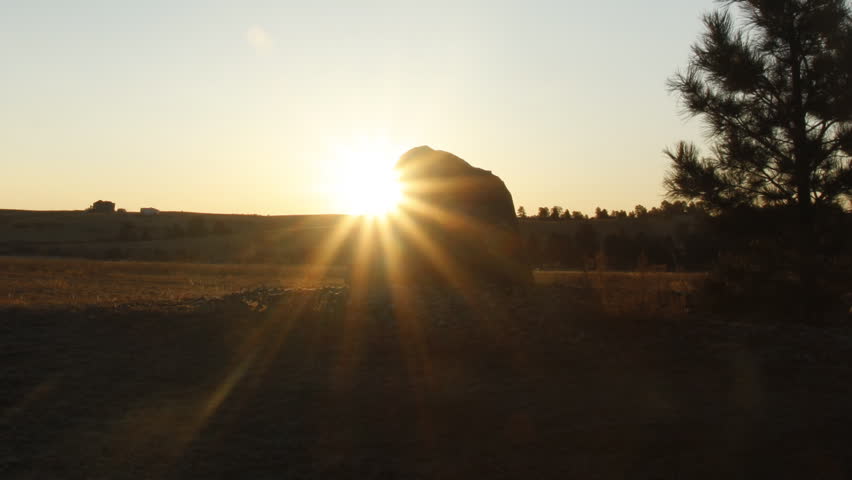 Time lapse of sunrise over a rock in a meadow, with brilliant sun rays extending