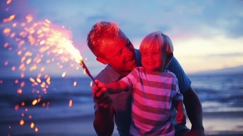 Father and son lighting sparklers on the beach at sunset