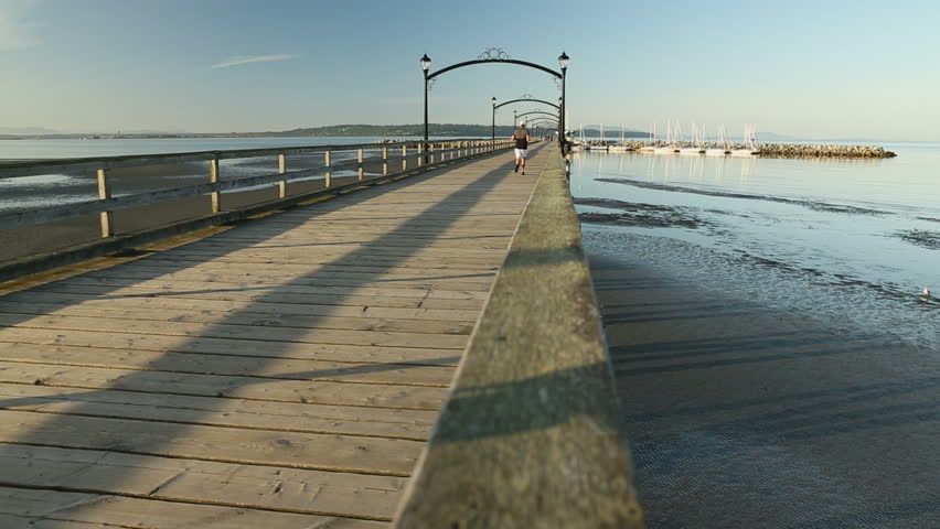 A jogger on the White Rock pier and the marina at the end of it. White Rock is a popular tourist destination on the west coast of British Columbia near the United States border.