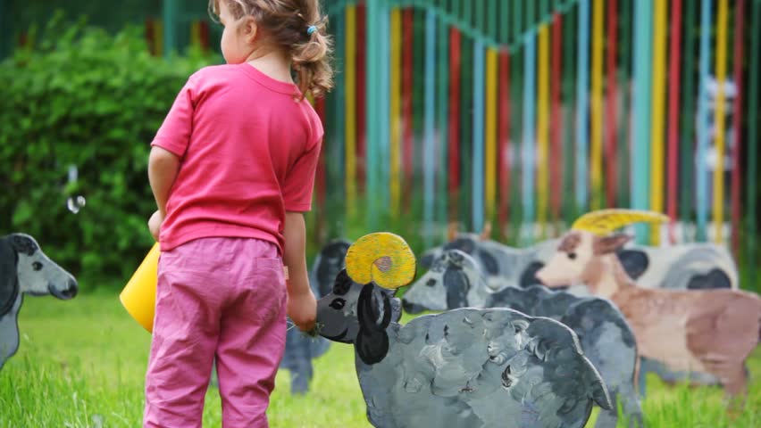 girl goes on lawn and feed from bowls with grass drawn silhouette of nanny-goat 