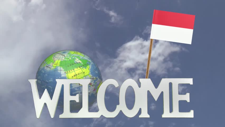 The word WELCOME in front of a turning globe and moving clouds in a blue sky with tooth pick and a small paper flag of INDONESIA