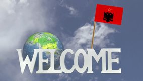 The word WELCOME in front of a turning globe and moving clouds in a blue sky with tooth pick and a small paper flag of ALBANIA