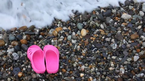 children's pink slippers on pebble beach with sea surf  Vídeo Stock