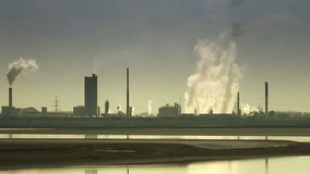 Smoke pouring from chimneys of petrochemical plant with river in foreground - Powered by Shutterstock - Get 15% off with code: PIKWIZARD15