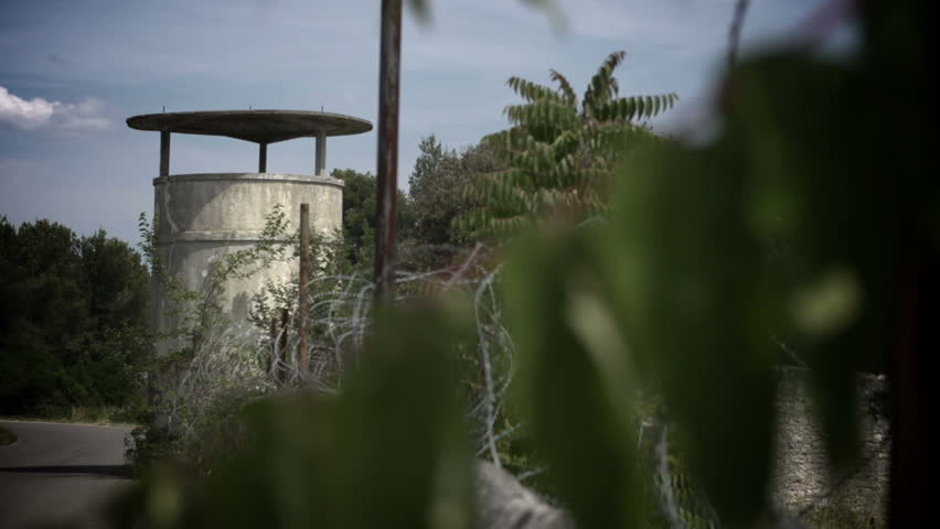 Dolly shot of military watchtower and wall, topped with razor wire