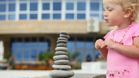 little blonde girl destroying stack of stones outdoor 