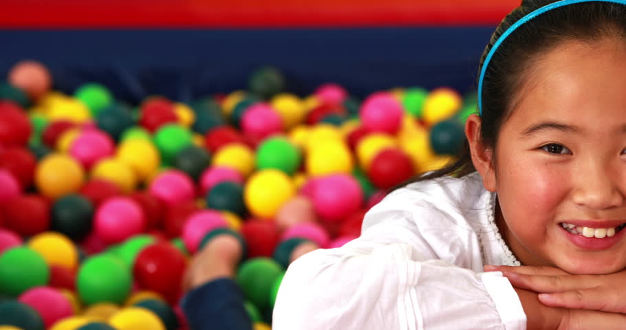 Portrait of cute Asian girl smiling at camera in ball pool in playschool