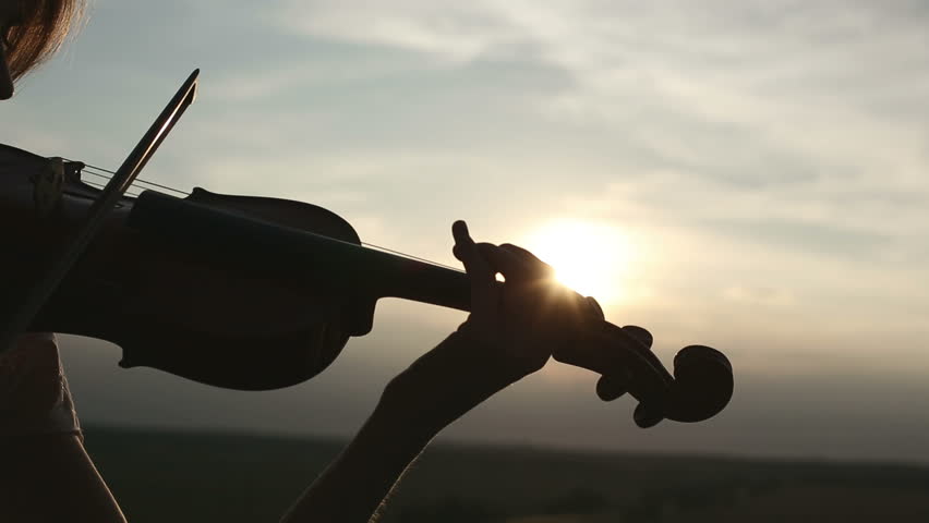 Silhouette girl violinist playing the violin at sunset sky background. Close up. Color v.2