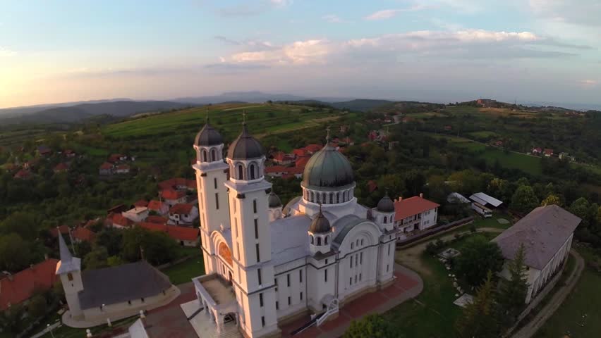 Aerial view over cathedral on countryside in mountains at sunset - establishing shot