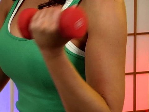 Close-up of the biceps of a lovely young brunette as she works with hand weights.  Camera zooms out to a medium shot. 
