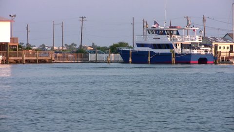 Video of a fishing sport boat crossing in front of a fishing dock, restaurant and marina. Blue water ocean bay channel with tour, sport and fishing boats in dock