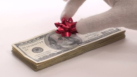 Generous Santa places festive bow on stack of hundred dollar bills isolated on white