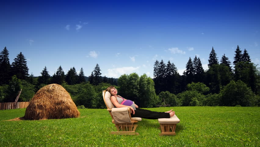 Pregnant woman in rocking chair on green meadow