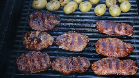 Barbecue pork chops being flipped on a grill with potatoes. 1080p BBQ grilling shots.