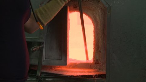 Glassblower pulls hot molten glass from the crucible of a glass furnace