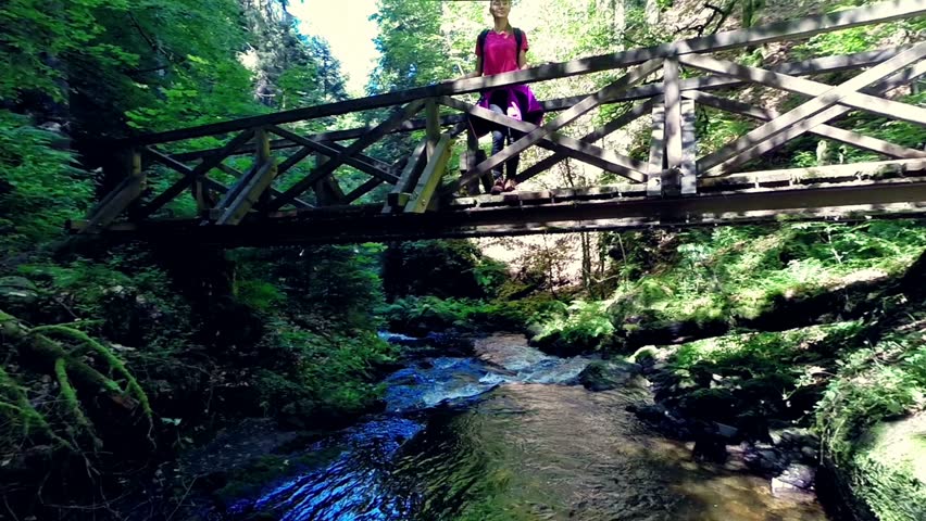 young hiker standing on a bridge, looking at landscape